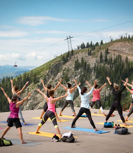 An outdoor yoga class on a mountaintop deck above the valley