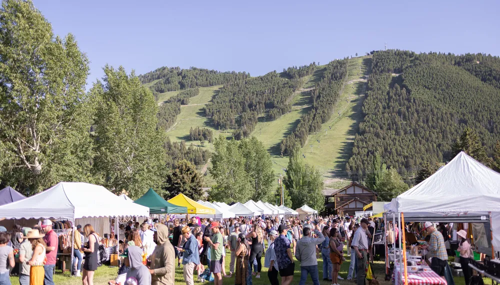 A summer crowd among white tents on the lawn below the Snow King ski runs